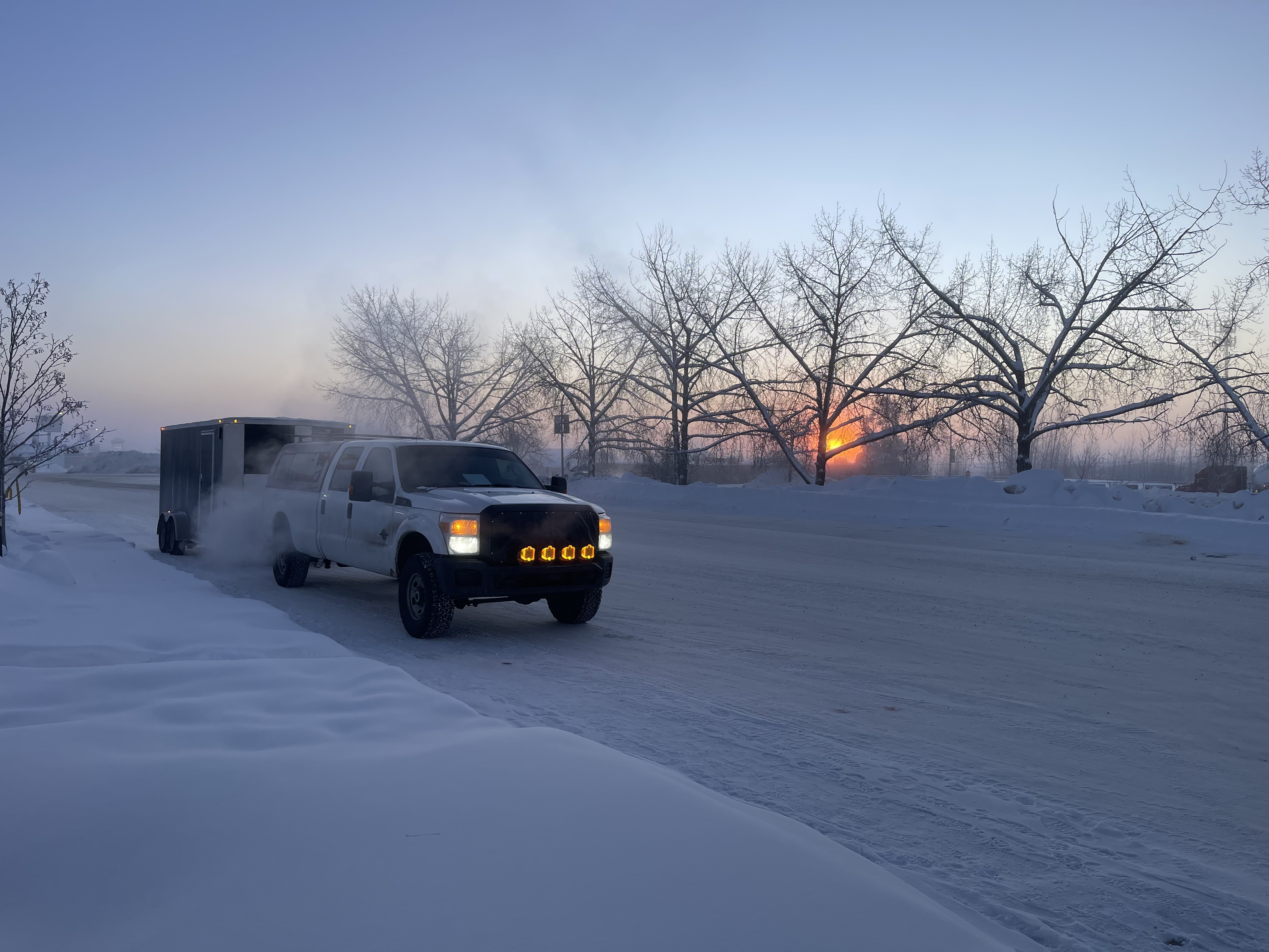 Dirigo pickup truck towing an enclosed trailer on a snowy road at sunrise